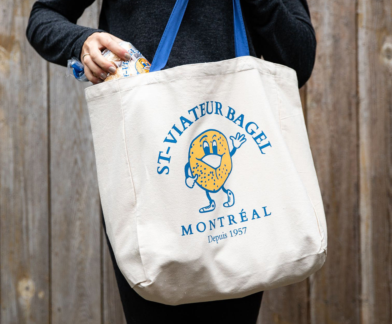 Person putting a bag of bagels into a branded St-Viateur tote bag.